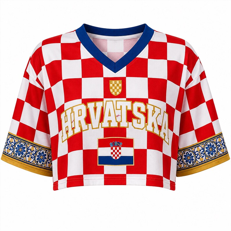 Pu&ograve; includere: Un top corto a maniche corte con un motivo a scacchi rosso e bianco. La parte anteriore presenta la scritta HRVATSKA in lettere dorate, un piccolo stemma e la bandiera croata. I bordi delle maniche hanno una decorazione floreale blu e oro.