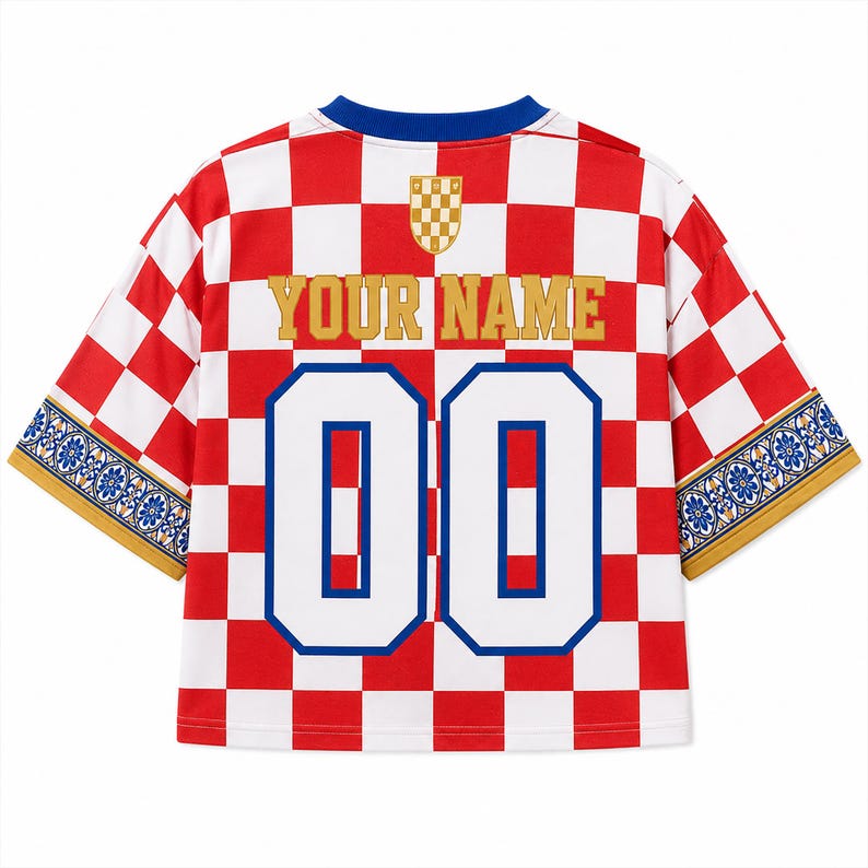 Pu&ograve; includere: Una maglia a maniche corte con motivo a scacchi rosso e bianco, scollo rotondo blu e la scritta "YOUR NAME" in oro sopra il numero "00" in bianco con bordi blu. Le maniche presentano un bordo floreale decorativo blu e bianco.