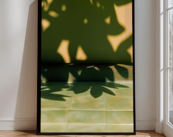 May include: Framed art print showing a close-up of a wall with green tiles and a shadow of leaves. The upper section of the print shows a tan wall with leaf shadows. The print is in a black frame.