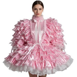 May include: A pink satin dress with multiple ruffled layers and white lace trim. The dress features a high collar, long sleeves, and a white ribbon detail. The overall design is ornate and feminine.