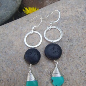 May include: Silver dangle earrings with black lava rock and turquoise stones. The earrings feature a silver hoop and a silver drop with a turquoise stone.