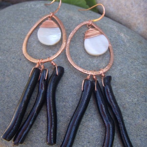 May include: Copper earrings with a white shell pendant and black tassel fringe.