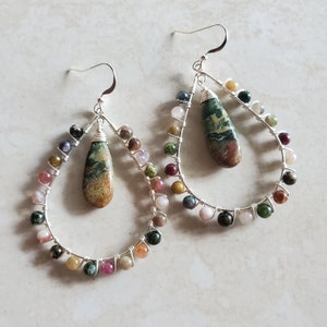 May include: A pair of silver wire earrings with a teardrop-shaped green, brown, and white stone hanging from each. The earrings are adorned with a variety of colorful beads, including pink, green, blue, and orange.