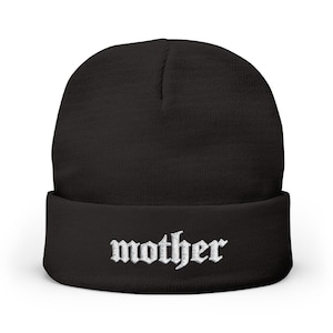 May include: Black beanie with the word "mother" embroidered in white gothic lettering across the folded brim. The beanie is made of a soft, knitted material and is designed to be worn on the head.