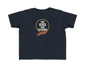 May include: Navy blue t-shirt featuring the text "THE KIDS ARE TALKING" inside a gold circle, with a rainbow design below. The shirt is made of a soft material.