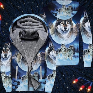 Puede incluir: Una sudadera con capucha con un diseño de lobos. El diseño presenta una manada de lobos en un paisaje nevado bajo la luna llena. La sudadera tiene un fondo azul, una capucha forrada de forro polar gris y una cremallera completa.