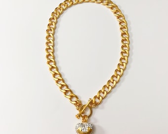 May include: Gold-toned chain necklace with a heart-shaped pendant. The pendant is encrusted with clear crystals and features a smiling face design. The necklace has a toggle clasp closure and is displayed on a white background.