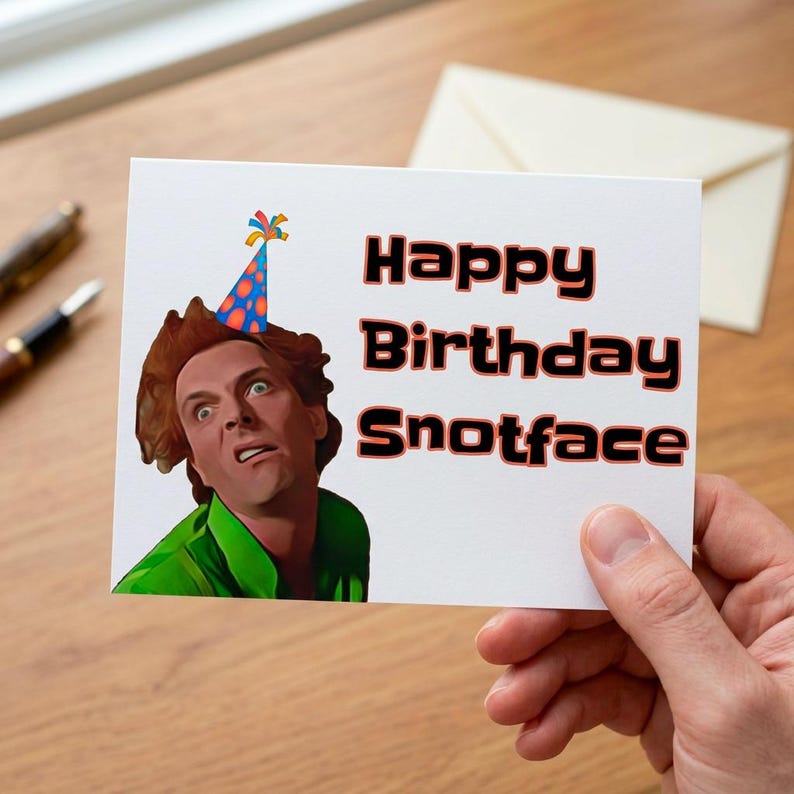 Puede incluir: Una tarjeta de felicitaci&oacute;n blanca con el texto "Happy Birthday Snotface" en negro y rojo. La tarjeta presenta una imagen de dibujos animados de un hombre con un gorro de fiesta y una camisa verde. La tarjeta est&aacute; sujeta por una mano.