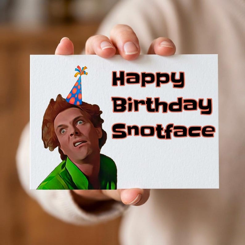 Puede incluir: Una tarjeta de felicitaci&oacute;n blanca sostenida por una persona, con el texto "Happy Birthday Snotface" en negro y rojo. La tarjeta tiene una ilustraci&oacute;n de una persona con un gorro de fiesta y una camisa verde.