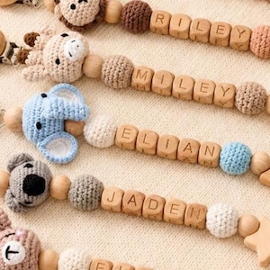 Peut inclure: Six attaches-sucettes personnalisées avec des perles en bois, des têtes d'animaux crochetées et des embouts en forme d'étoile. Chaque attache porte un prénom : CHLOE, RILEY, MILEY, ELIAN, JADEN et ELLIE, avec des clips métalliques et des boucles.
