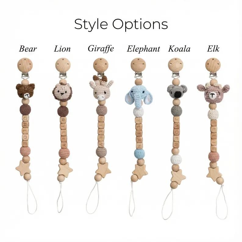 Op de afbeelding: Houten fopspeenclips met gehaakte dierenkoppen, waaronder een beer, leeuw, giraf, olifant, koala en eland. Elke clip heeft een houten ster en gepersonaliseerde naamkralen. De tekst "Style Options" staat bovenaan.