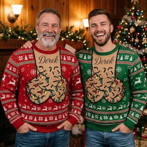 May include: A red and a green long-sleeve knit jumper, each featuring a tan rectangular panel on the chest with the name Derek printed in black script. The design includes two illustrated cookies wrapped in colourful Christmas lights.