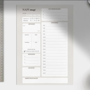 Puede incluir: Un planificador diario con el texto "NAPI tervező" en la esquina superior izquierda. El planificador tiene secciones para la fecha, el estado de ánimo, listas de tareas y un horario de 6:00 a 22:00. También se ven una regla de metal, un bolígrafo y una taza de café.