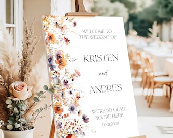 Pode incluir: Uma placa de boas-vindas de casamento branca em um cavalete de madeira. A placa apresenta obras de arte florais em tons de laranja, roxo e rosa. O texto diz: "Bem-vindos ao casamento de Kristen e Andres. Ficamos felizes que você esteja aqui. 09.21.2030."