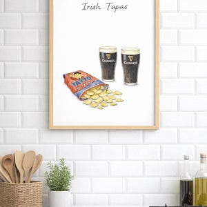 May include: A framed print depicting two pints of Guinness, a packet of Tayto cheese and onion crisps, and the words "Irish Tapas." The image is set against a white brick wall, suggesting a pub or kitchen setting.