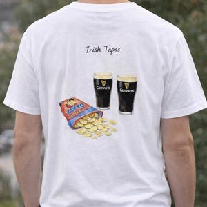 May include: White t-shirt with an illustration of Irish tapas. The design includes two glasses of Guinness, a bag of Tayto crisps, and the words "Irish Tapas". The shirt is a casual wear item.