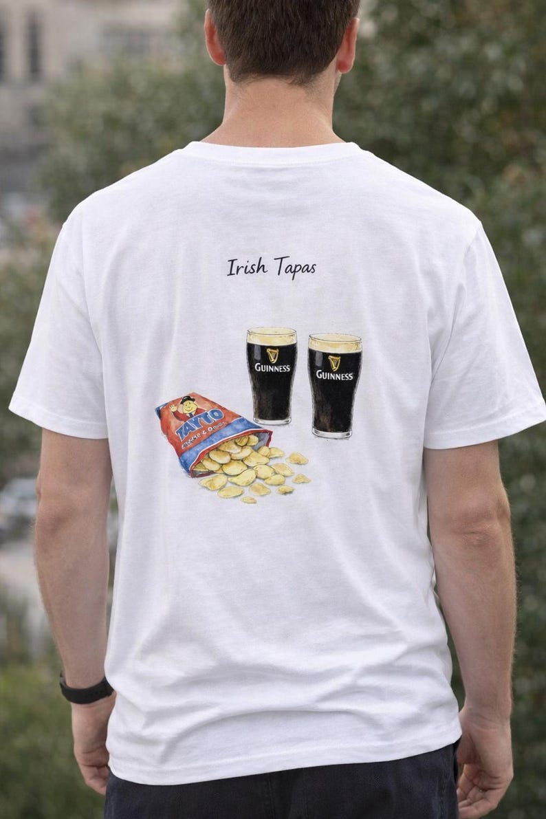May include: White t-shirt with an illustration of Irish tapas. The design includes two glasses of Guinness, a bag of Tayto crisps, and the words "Irish Tapas". The shirt is a casual wear item.