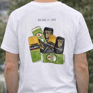 Pu&ograve; includere: T-shirt bianca con una grafica di diverse lattine di birra e sidro, tra cui Heineken, Guinness e Bulmers. Il testo "BIG BAG OF CANS" &egrave; stampato sopra le lattine.