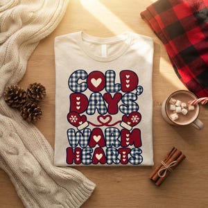 Peut inclure: Un t-shirt couleur crème avec le texte COLD DAYS WARM HEARTS dans un mélange de motifs à carreaux rouges et bleus. Le design comprend des moufles rouges avec des flocons blancs, des petits cœurs blancs et un cœur rouge reliant les mots.