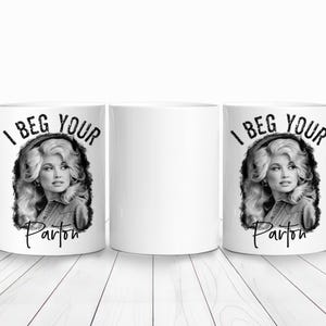 Könnte beinhalten: Weiße Keramik-Tasse mit einem Schwarz-Weiß-Porträt einer Frau und dem Text "I BEG YOUR Parton". Die Tasse hat einen Henkel und wird auf einer weißen Holzoberfläche präsentiert. Ein Neuheitenartikel.