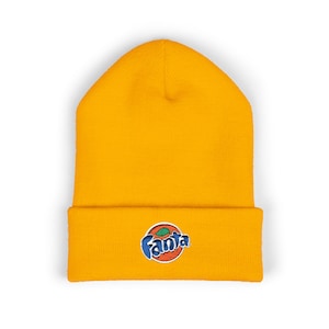 May include: Mustard yellow beanie with a folded brim. The beanie features a colorful embroidered Fanta logo on the front. The logo includes the word "Fanta" in blue script, with a stylized orange and green graphic.