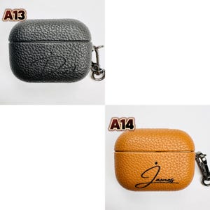 May include: Two leather AirPod cases are shown. One is black with the name "James" in cursive, and the other is tan with the same name. Both cases have a textured surface, a silver clasp, and the labels "A13" and "A14".