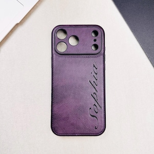 Pode incluir: Capa de telefone roxa com recortes para a câmera e o nome "Sophia" em escrita cursiva. A capa tem uma aparência texturizada semelhante ao couro. A capa foi projetada para proteger a câmera e o corpo do telefone.