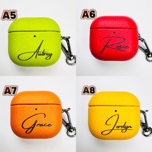 May include: Four colorful AirPod cases are displayed, each with a different name in cursive script. The cases are lime green with "Aubrey", red with "Rosie", orange with "Grace", and yellow with "Jordyn". Each case has a black carabiner clip.