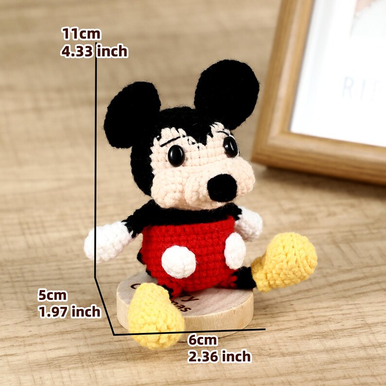 May include: A handmade crochet Mickey Mouse figure. The figure is black, red, white, and yellow. It measures 4.33 inches tall, 1.97 inches wide, and 2.36 inches long. The figure is sitting on a small wooden base.