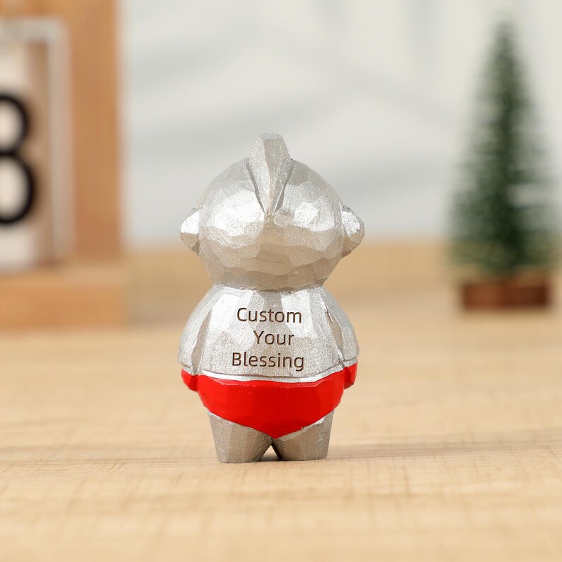 May include: A silver-colored figurine of a cartoon character with a red bottom. The text "Custom Your Blessing" is printed on the character's back. The figurine is standing in front of a blurred background.