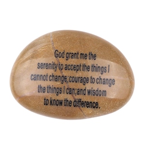 Op de afbeelding: Een gladde, ovaalvormige, bruingekleurde steen met een lichtbruine ader. De steen bevat de tekst "God, geef me de sereniteit om de dingen te accepteren die ik niet kan veranderen, de moed om de dingen te veranderen die ik kan, en de wijsheid om het verschil te kennen."