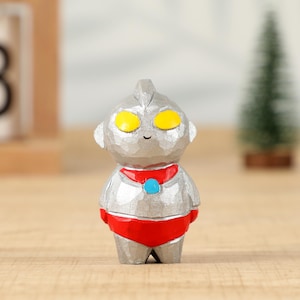 May include: A silver-colored figurine of a cartoon character with yellow eyes, a red collar, and red shorts. The figurine has a textured surface and a small smile. The character is standing on a wooden surface.