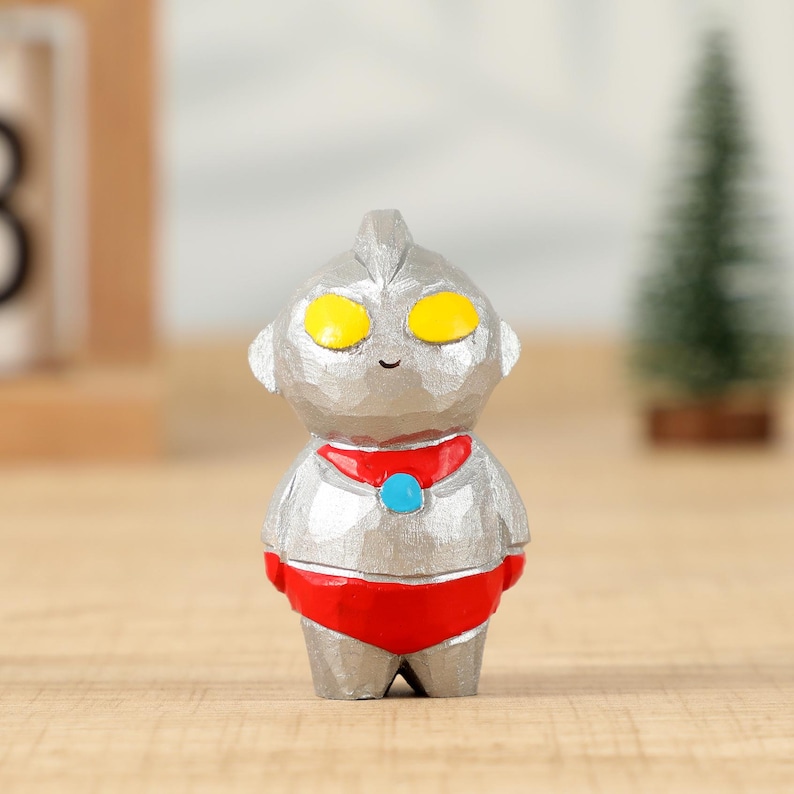 May include: A silver-colored figurine of a cartoon character with yellow eyes, a red collar, and red shorts. The figurine has a textured surface and a small smile. The character is standing on a wooden surface.