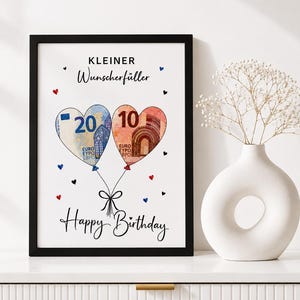 Può includere: Una stampa incorniciata con il testo KLEINER Wunscherfüller e Happy Birthday. Il design mostra due palloncini a forma di cuore realizzati con banconote da 20 e 10 euro, legati insieme da un fiocco nero e circondati da piccoli cuori rossi e blu.