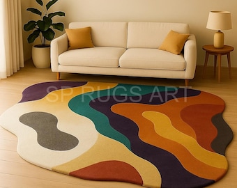 May include: A colorful, abstract area rug with a unique, organic shape. The rug features a flowing design with shades of purple, teal, orange, yellow, and cream. The text "SP RUGS ART" is visible on the rug. The rug is placed in a living room setting.