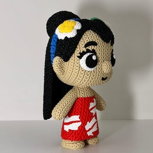 Puede incluir: Mu&ntilde;eca hecha a mano con cara y cuerpo bronceados, cabello negro y un vestido rojo con detalles blancos. La mu&ntilde;eca tiene ojos negros grandes y una flor en el pelo. La mu&ntilde;eca est&aacute; sobre una superficie blanca.