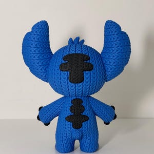 Puede incluir: Figura azul de un personaje de dibujos animados con orejas grandes y detalles negros. La figura tiene un aspecto texturizado y tejido. Los brazos del personaje est&aacute;n levantados y tiene una nariz y ojos peque&ntilde;os y negros.
