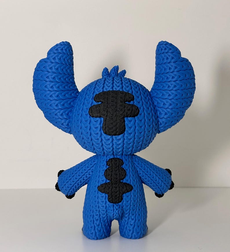 Puede incluir: Figura azul de un personaje de dibujos animados con orejas grandes y detalles negros. La figura tiene un aspecto texturizado y tejido. Los brazos del personaje est&aacute;n levantados y tiene una nariz y ojos peque&ntilde;os y negros.