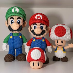 May include: Four knitted figures of characters from the Super Mario video game series. Mario and Luigi are in their signature outfits, with red and green hats, blue dungarees, and black moustaches. A Toad and a mushroom are also present.
