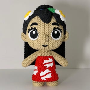 Puede incluir: Mu&ntilde;eca hecha a mano que representa a un personaje con cabello negro, ojos grandes y un vestido rojo con detalles blancos. La mu&ntilde;eca tiene una textura de punto y est&aacute; adornada con detalles florales coloridos en el cabello. La mu&ntilde;eca est&aacute; de pie.