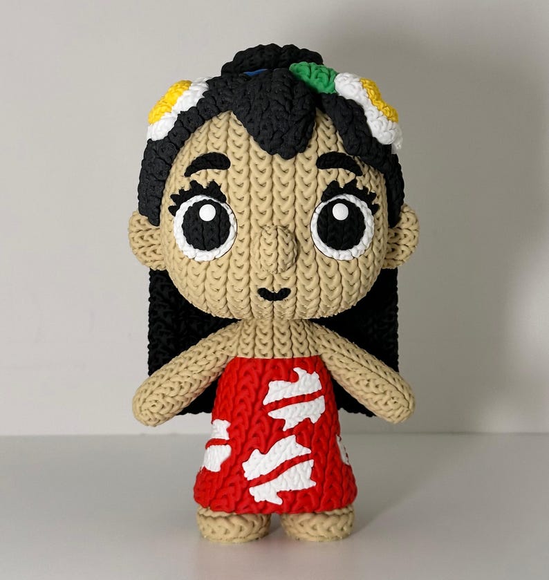 Puede incluir: Mu&ntilde;eca hecha a mano que representa a un personaje con cabello negro, ojos grandes y un vestido rojo con detalles blancos. La mu&ntilde;eca tiene una textura de punto y est&aacute; adornada con detalles florales coloridos en el cabello. La mu&ntilde;eca est&aacute; de pie.