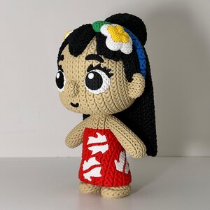 Puede incluir: Mu&ntilde;eca hecha a mano que representa a un personaje con cabello negro, un vestido rojo con detalles blancos y un accesorio floral para el cabello. La mu&ntilde;eca tiene ojos grandes y una apariencia tejida texturizada.