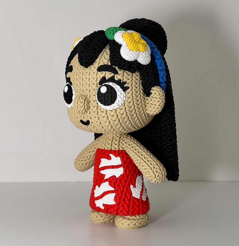 Puede incluir: Mu&ntilde;eca hecha a mano que representa a un personaje con cabello negro, un vestido rojo con detalles blancos y un accesorio floral para el cabello. La mu&ntilde;eca tiene ojos grandes y una apariencia tejida texturizada.