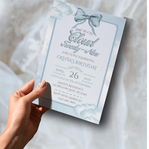 Puede incluir: Una tarjeta de invitación azul claro con un diseño de nube y lazo. El texto dice "She is on Cloud Twenty-Nine" e invita a los invitados al cumpleaños de Olivia el 26 de abril de 2025 a las 3 PM. Se incluye información de RSVP.