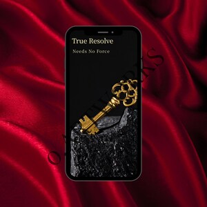 May include: A smartphone displays a gold key resting on a dark rock against a black background. The text "True Resolve Needs No Force" is at the top of the screen. The background is a deep red, silky fabric.