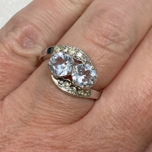 May include: A silver ring with two large clear stones and smaller clear stones around the band.