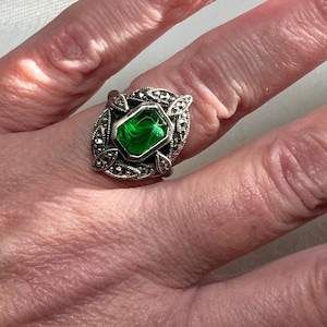 May include: A silver ring with a green gemstone set in a marquetry design.