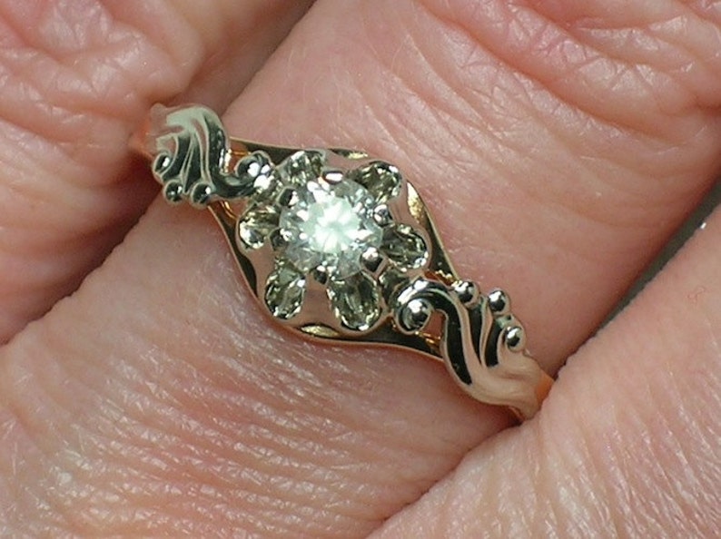 May include: A gold ring with a delicate, ornate design featuring a single, round, clear diamond in the center.