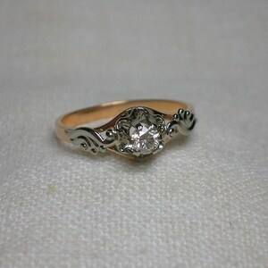 May include: A gold and silver ring with a single round diamond set in a floral design.