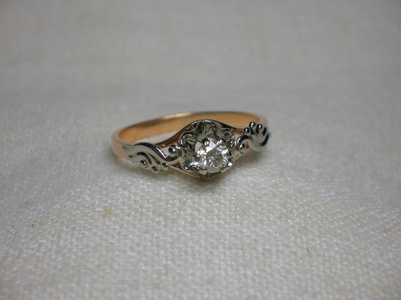 May include: A gold and silver ring with a single round diamond set in a floral design.